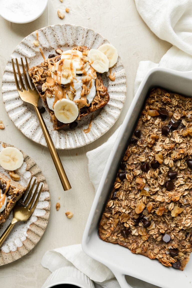 Overhead view of a pan of freshly baked banana chocolate chip baked oatmeal with a piece on a plate beside the pan drizzled with peanut butter.