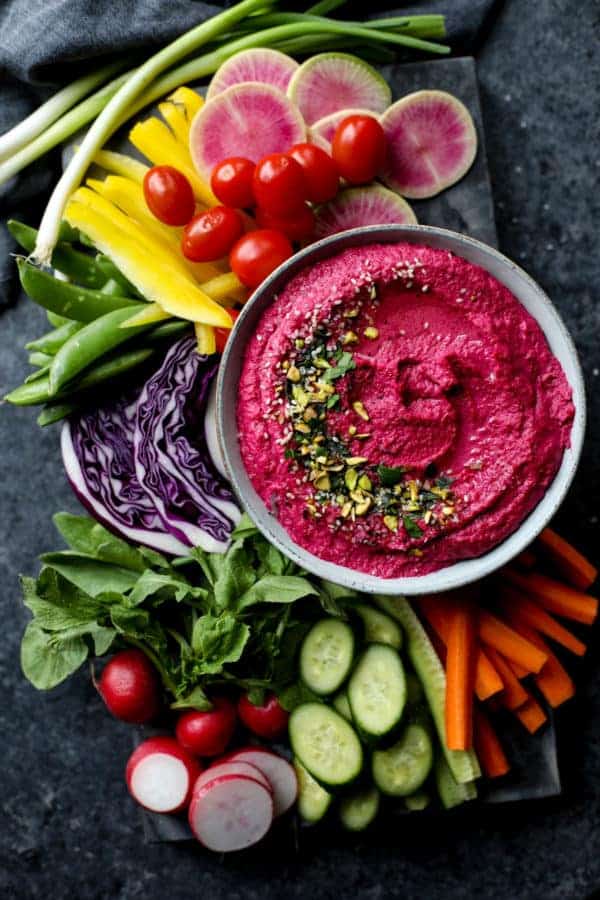 Overhead view of a colorful bowl of Beet Hummus surrounded by raw vegetables