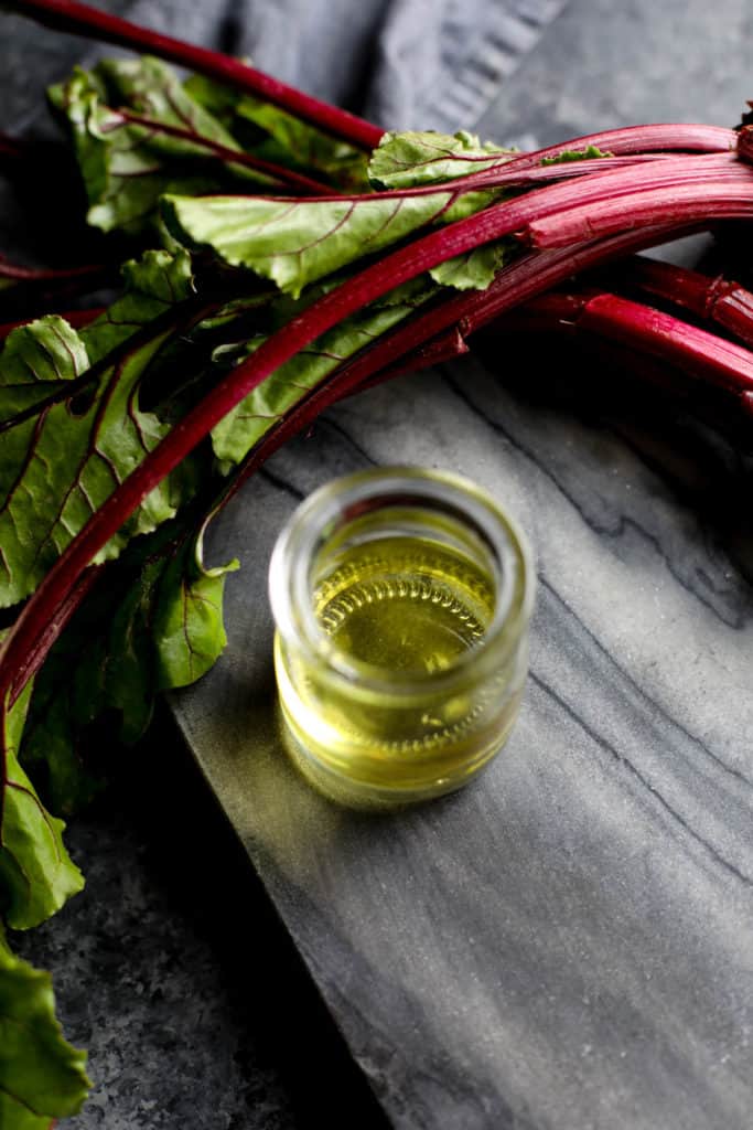 A cup filled with algae oil next to beet stems
