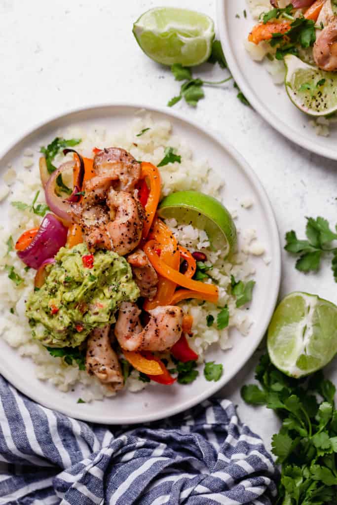 Plated fajita chicken over a bed of cauliflower rice, peppers, onions and guacamole with a lime garnish. 3 of 10 Quick and Easy Dinner Ideas.