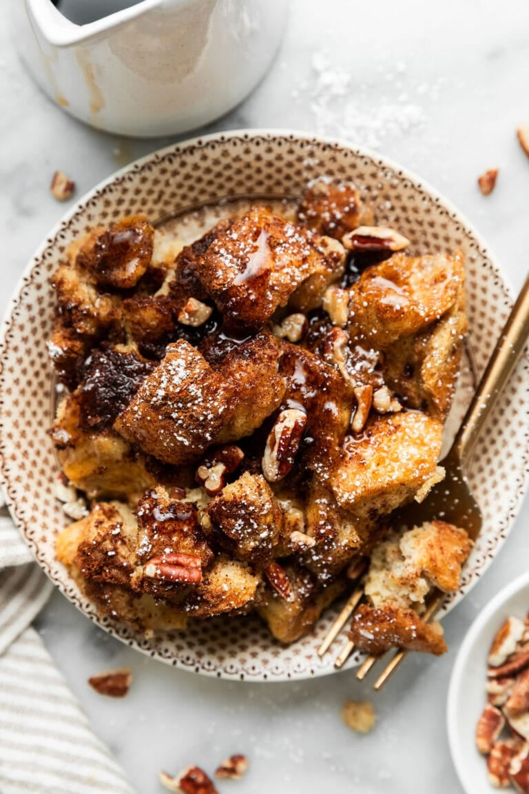 Overhead view of a plate of French toast casserole topped with pecans and maple syrup. 