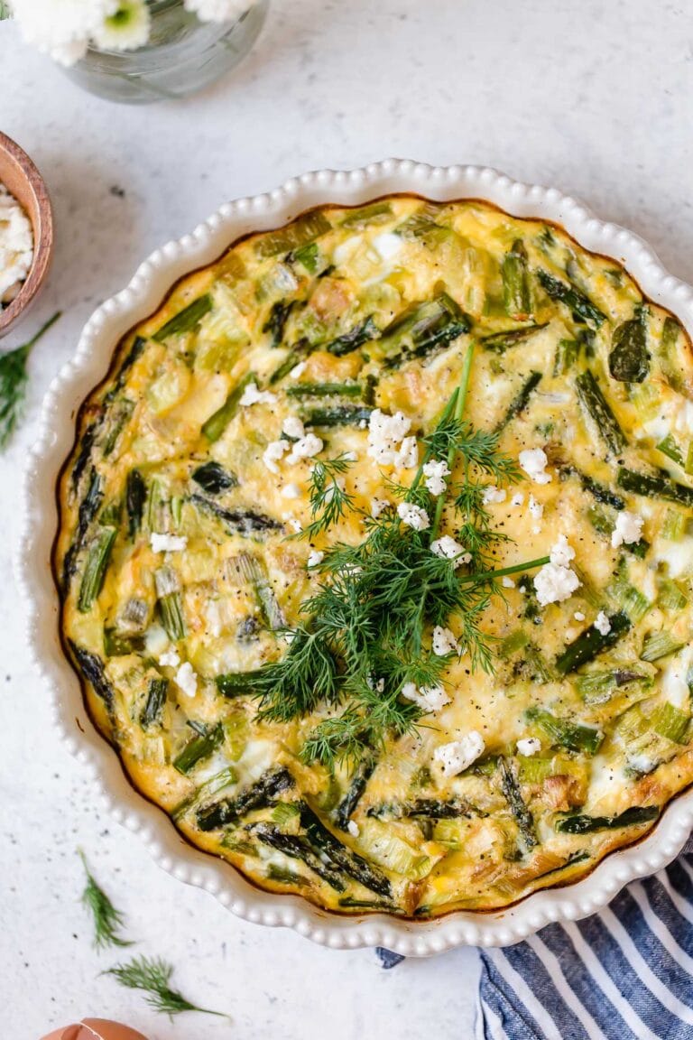 Overhead view of a pie pan filled with crustless asparagus quiche topped with feta and fresh dill.