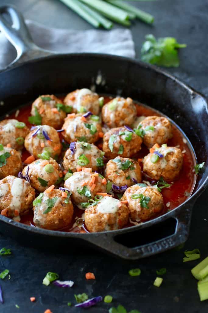 Iron skillet filled with meatballs and surrounded by sauce with veggie accents of purple, green and orange.