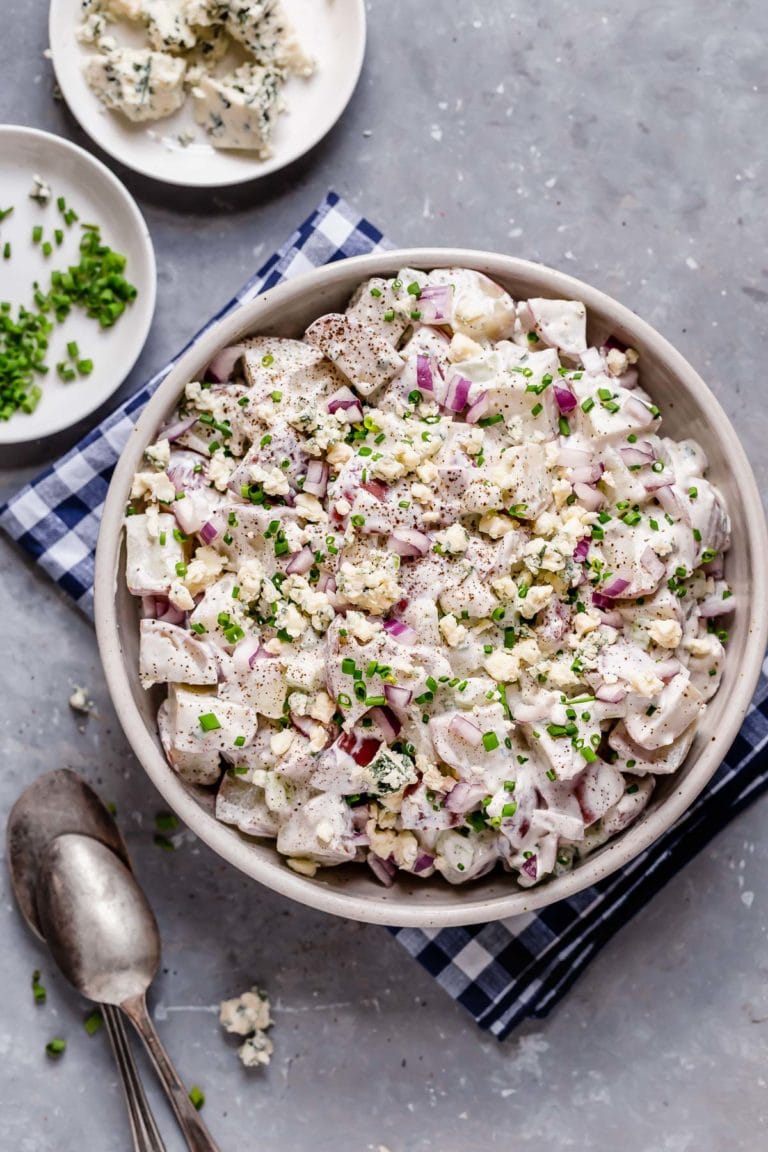 Overhead view of a creamy bowl of blue cheese potato salad with red onion, celery, and chives. 