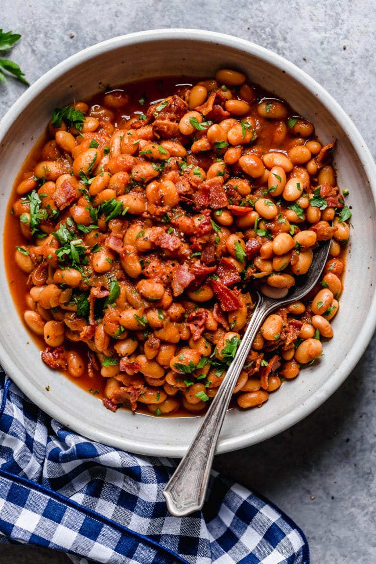 Overhead view of a large bowl of baked beans topped with fresh herbs and crisp bacon pieces.