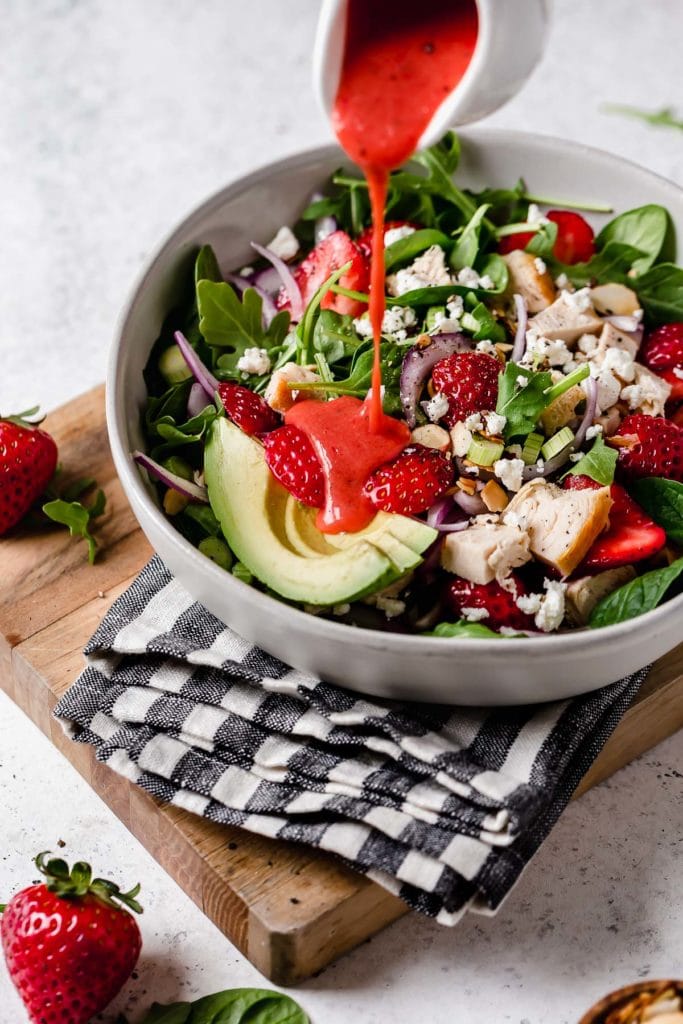 Overhead view of a bowl of Strawberry Vinaigrette being poured over a salad with chicken and greens
