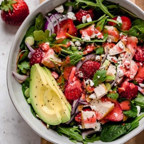 Spinach salad with chicken and strawberries in a white bowl