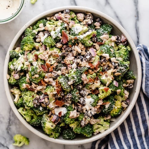 Overhead view white stone bowl filled with creamy broccoli salad topped with bacon