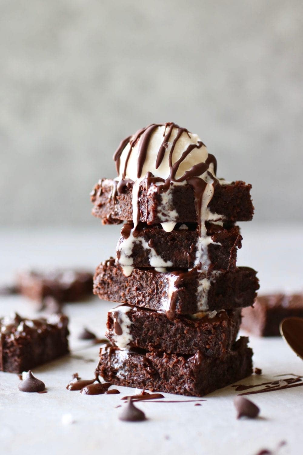 Photo of a stack of five Paleo Fudgy Brownies with a scoop of cream on top. Drizzled with chocolate.