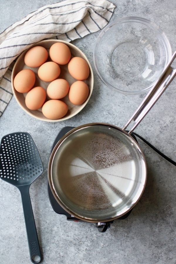 Overhead view of a bowl of brown eggs, water and a stainless-steel pan