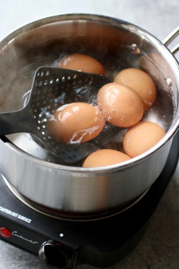 A slotted spoon scooping out Hard-Boiled Eggs from a pan