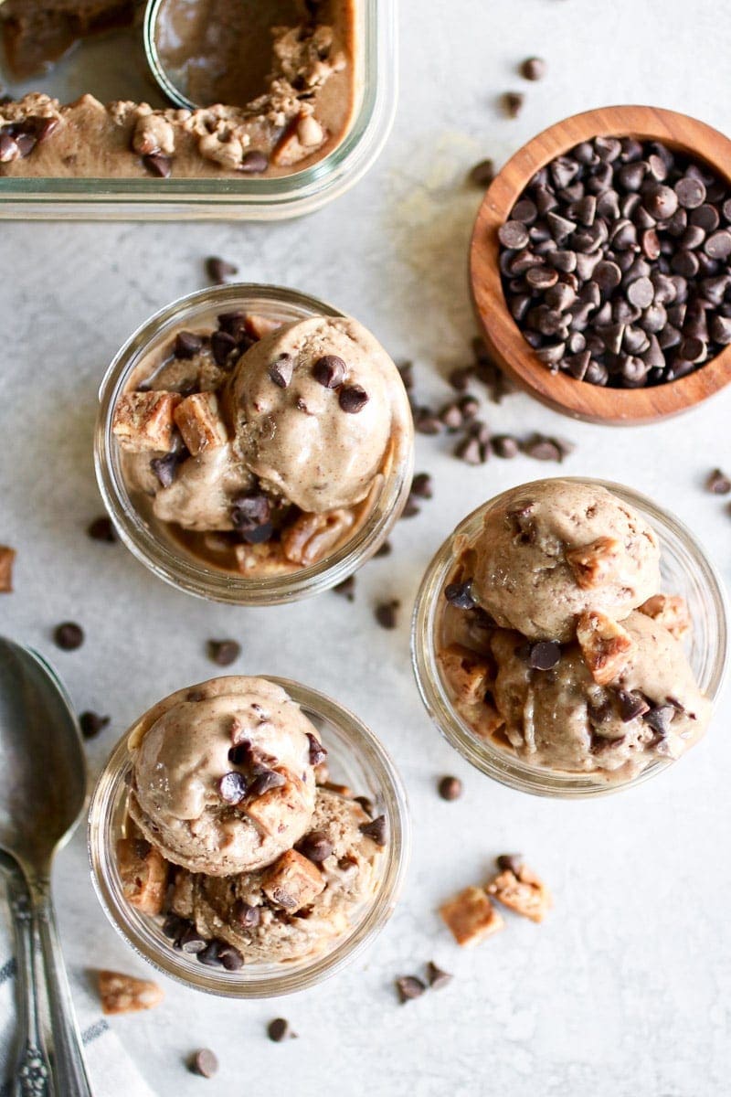 Photo of three servings of Almond Butter Banana Nice Cream served in a small mason jar topped with chocolate chips and pieces of Caveman Collagen Bar.