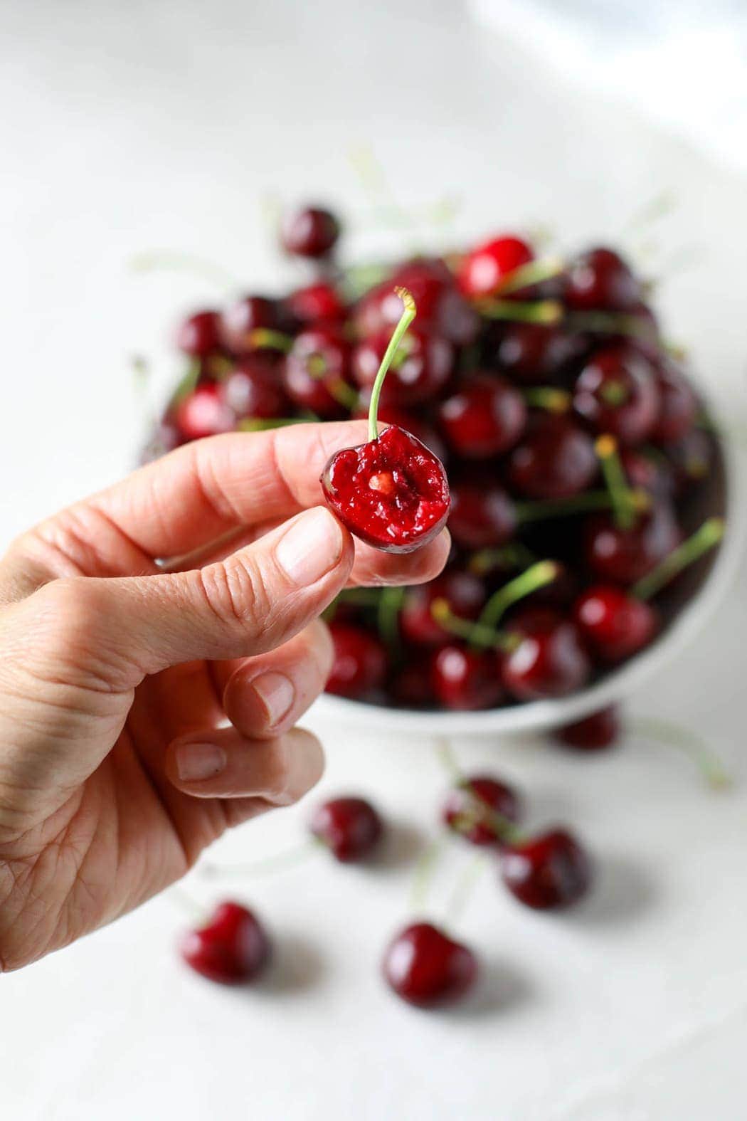 A hand holding a cherry with a bite out of it and exposing the pit inside.