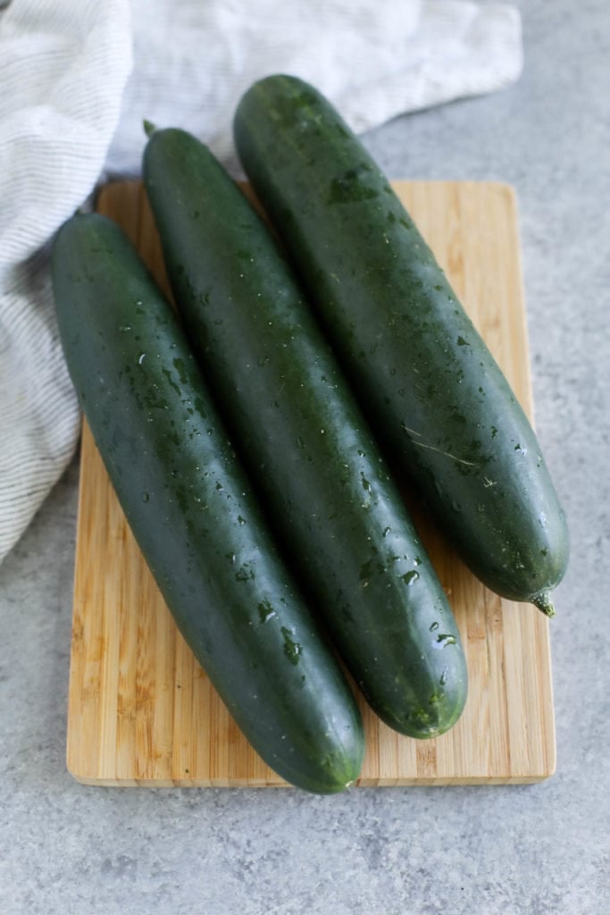 3 zucchinis laying in a row on a wood cutting board