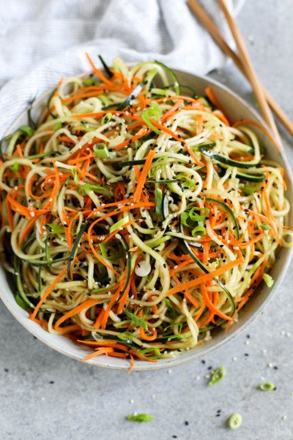 Overhead view of a white bowl filled with Asian-Inspired Cucumber “Noodle” Salad topped with sesame seeds and green onions