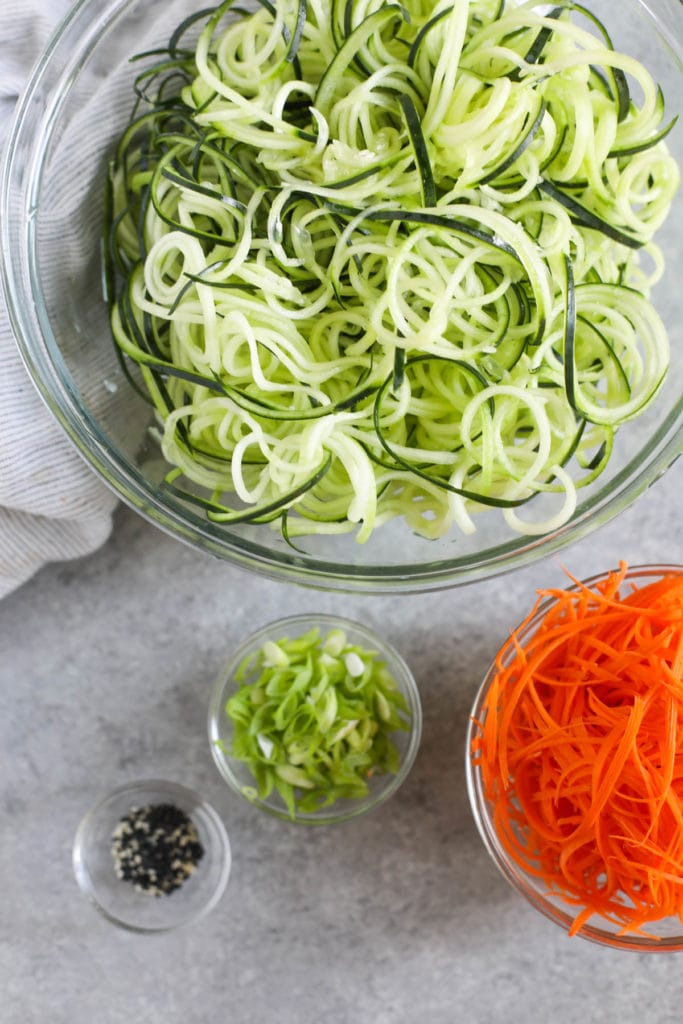 Overhead view of a glass bowl filled with zucchini noodles and carrot shreds in a bowl on the side