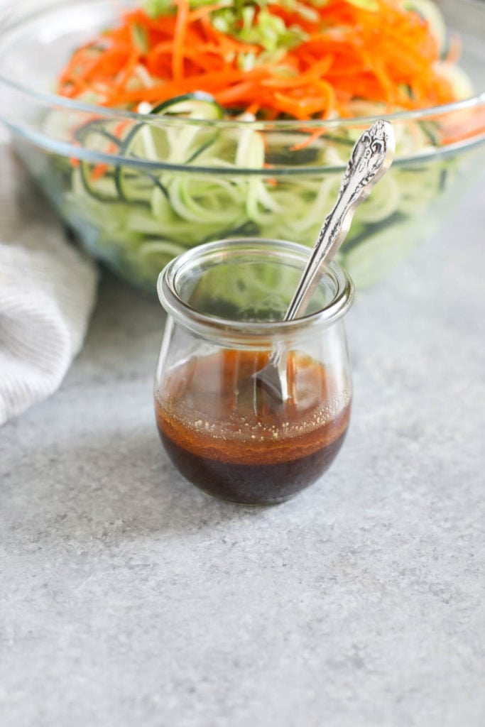 Close up view of a Asian-Inspired Cucumber “Noodle” Salad dressing in a small glass jar