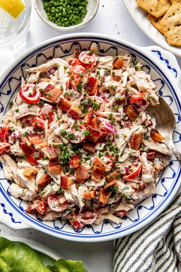 Overhead view of a bowl filled with BLT chicken salad and topped with fresh chives and crisp pieces of bacon.