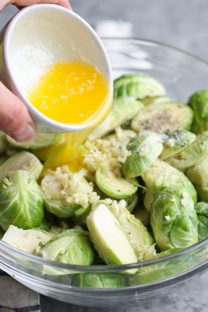 a bowl of brussels sprouts with oil being poured over them