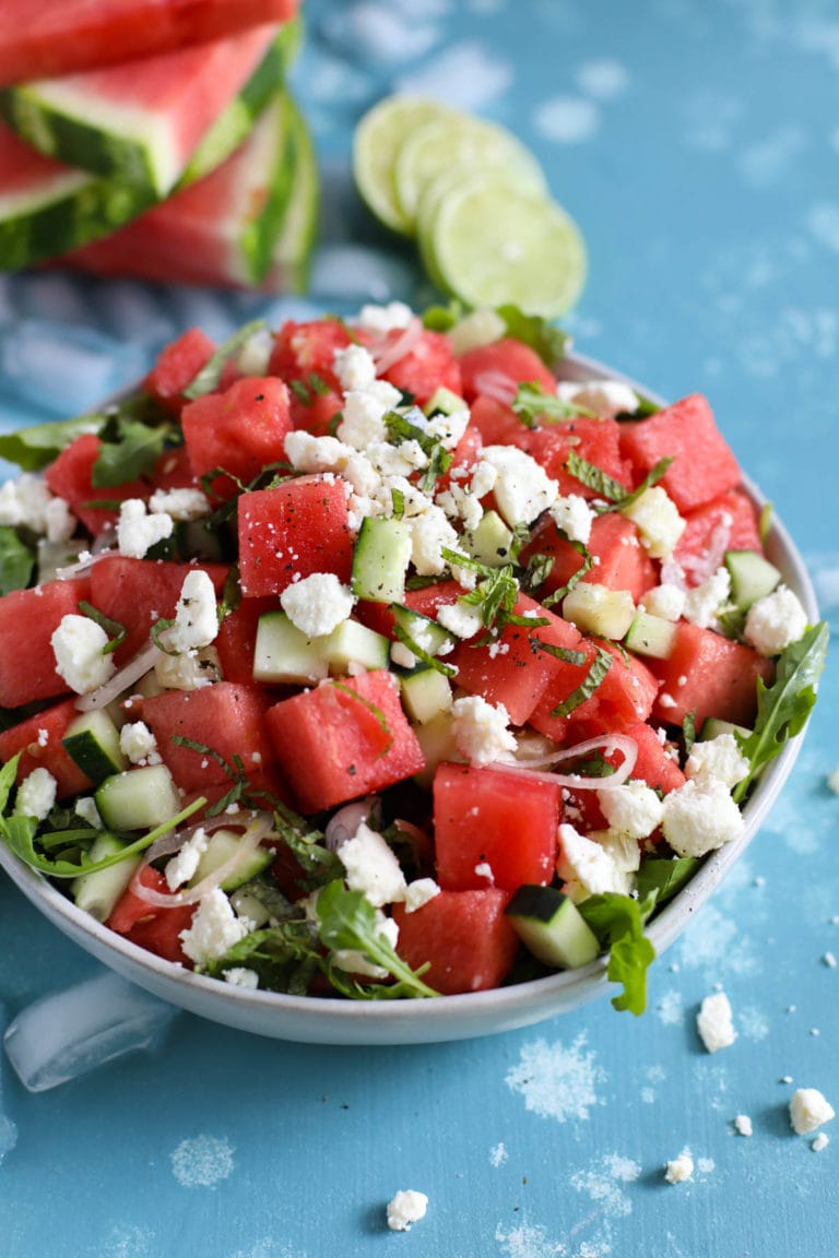 Overhead view of a colorful watermelon salad topped with salty feta cheese and a tart lime juice.