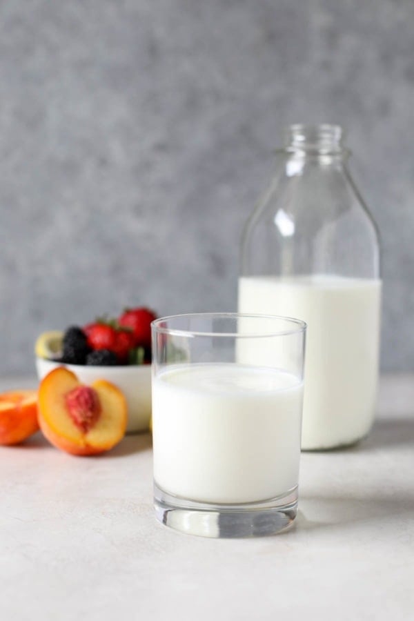 Close up view of a glass of kefir with fresh fruit in the background.