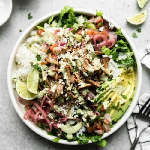 White bowl filled with rice, carnitas, lettuce and toppings