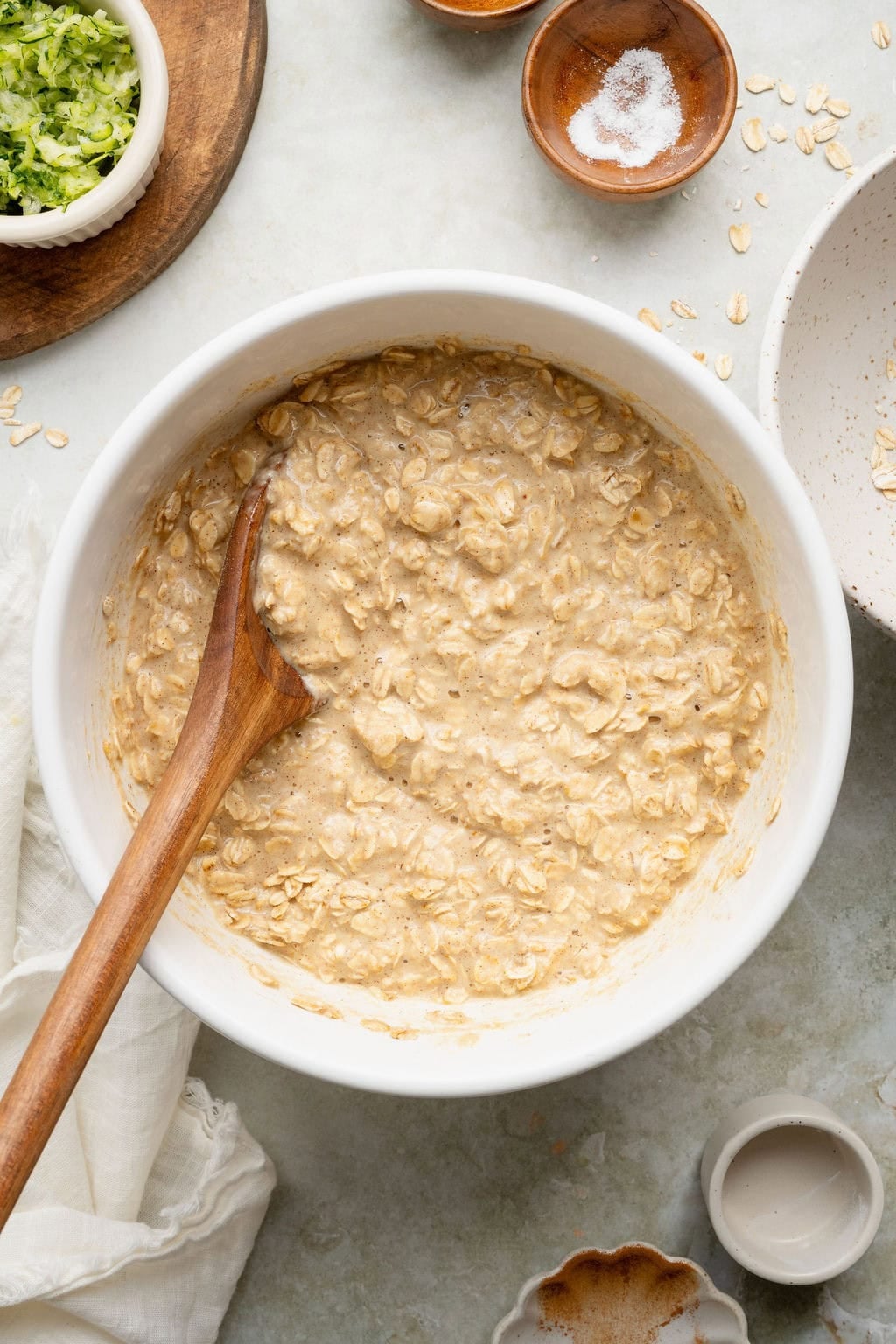 Mixed batter for baked oatmeal cups in a white bowl, a wooden spoon sticking out.