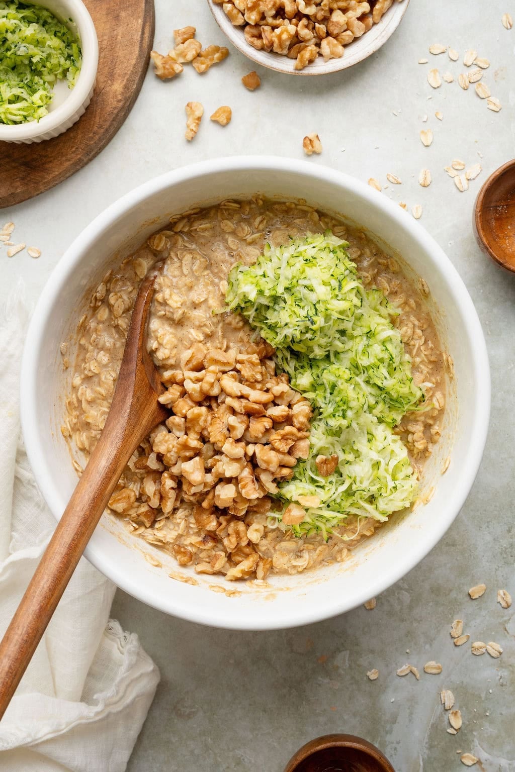 Walnuts and shredded zucchini being folded into a bowl of batter for breakfast oatmeal cups.