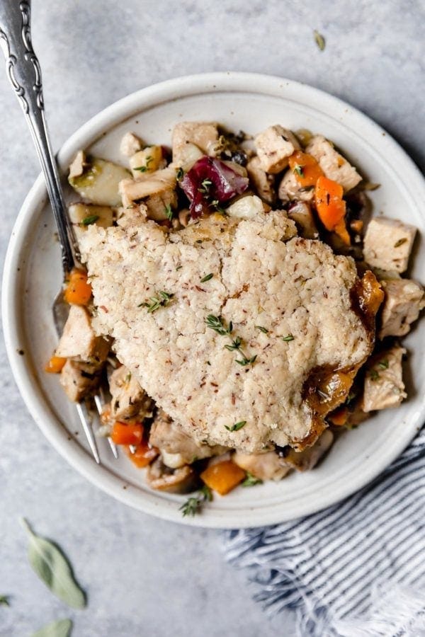 A overhead view of a plate of turkey and vegetables in a thyme-sage gravy is topped with a flaky grain-free pastry crust in this Paleo Turkey Pot Pie.