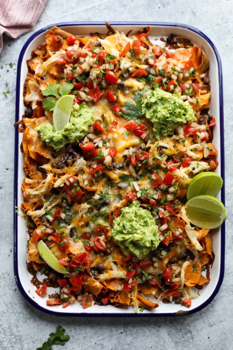 Overhead view of a baking dish filled with sweet potato nachos topped with melted cheese and guacamole.