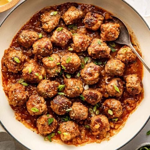 Overhead view of a skillet of sweet and sour meatballs sprinkled with sesame seeds.