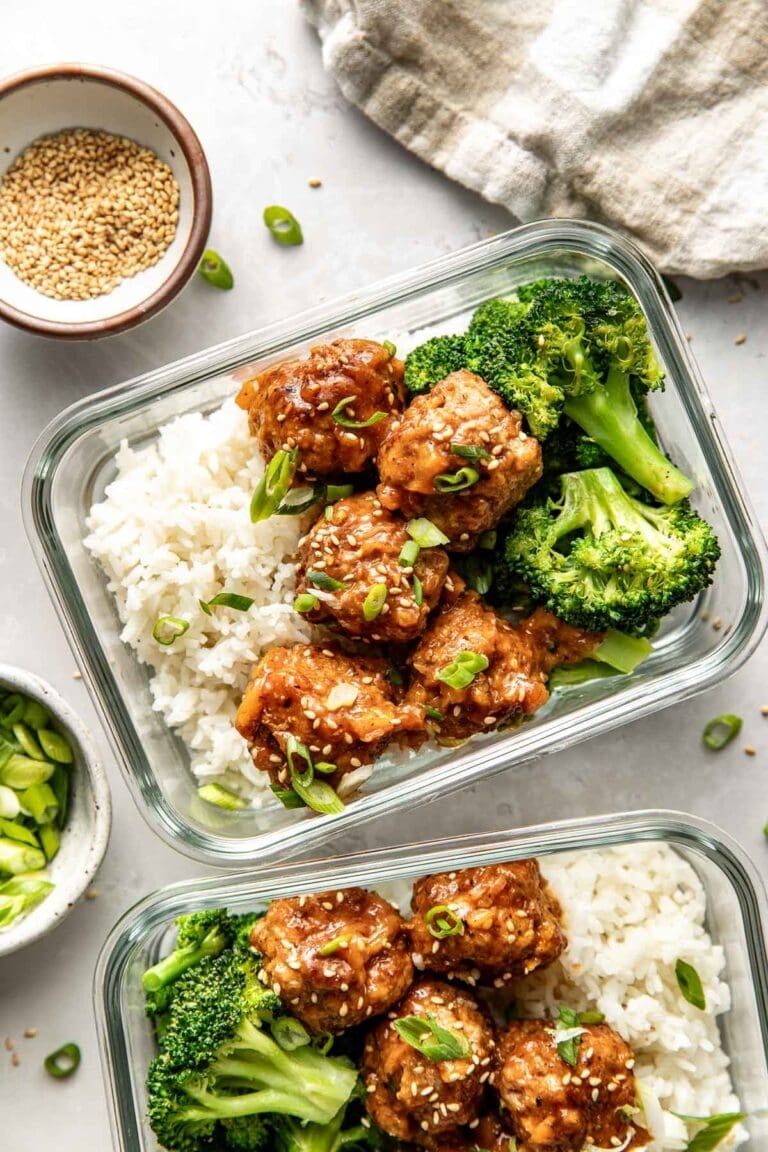 Overhead view of two glass meal prep containers filled with sweet and sour meatballs, white rice, and broccoli topped with sesame seeds and green onions.