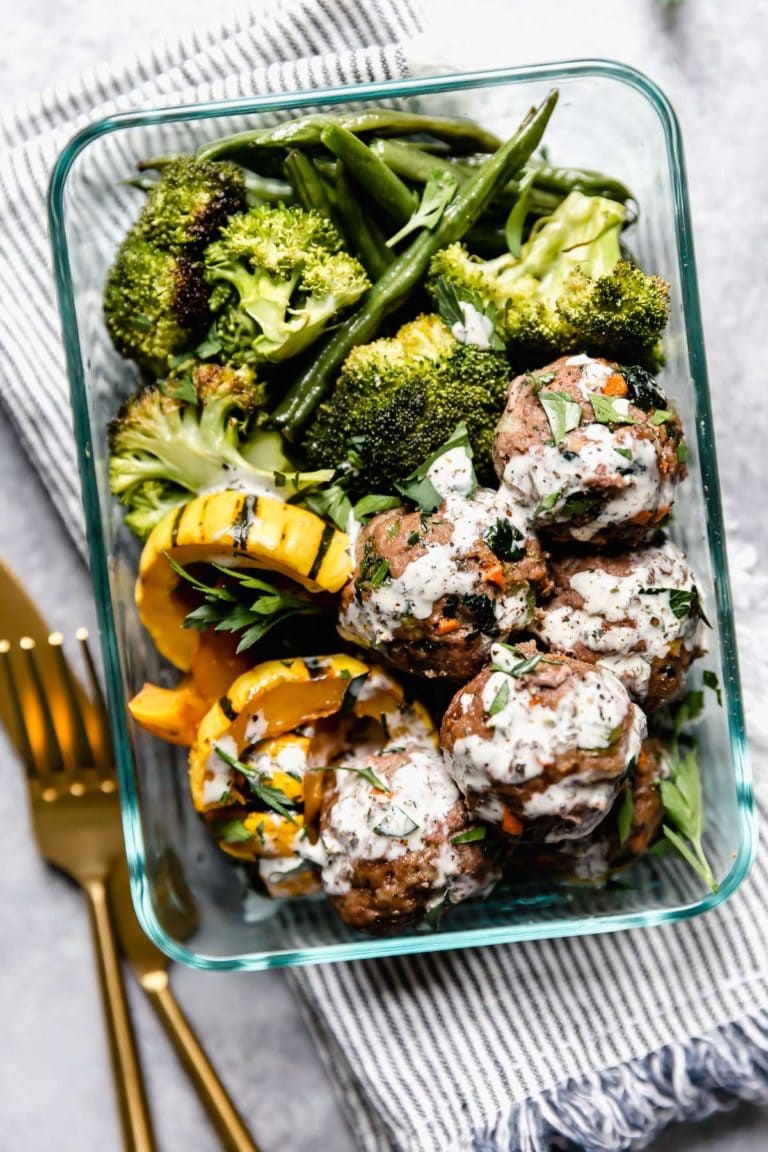 Overhead view glass meal prep container filled with meatballs and roasted veggies with ranch drizzled over top.