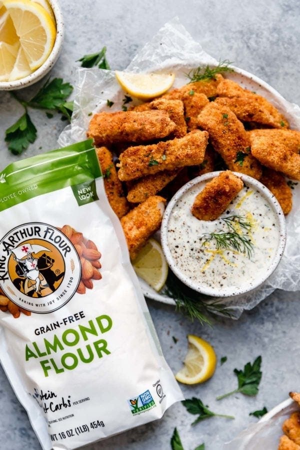 Overhead view of a plate of Baked Fish Sticks with Tartar Sauce with a bag of almond flour on the side.
