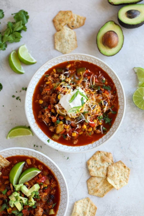 Overhead view of a bowl of Instant Pot Veggie Loaded Turkey Chili with limes and avocado around it