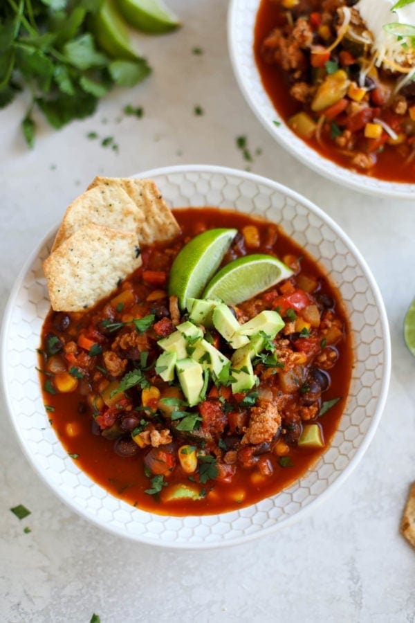 A white bowl of Instant Pot Veggie Loaded Turkey Chili topped with avocado and fresh herbs