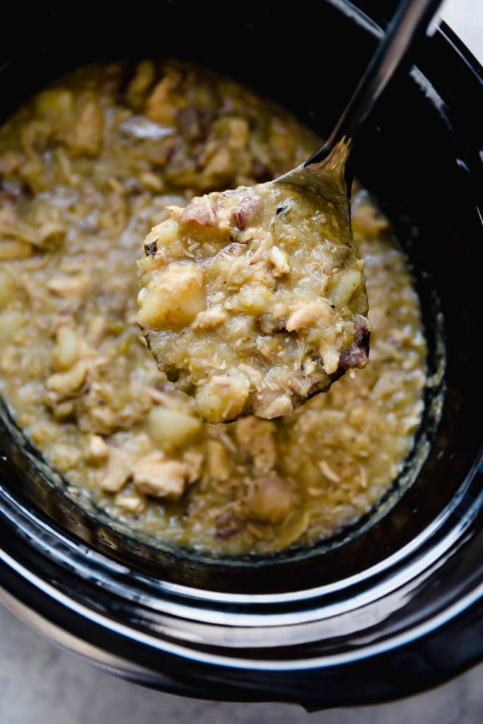 A spoon scoops a portion of Slow Cooker Chicken Chile Verde Stew out of a black slow cooker. 