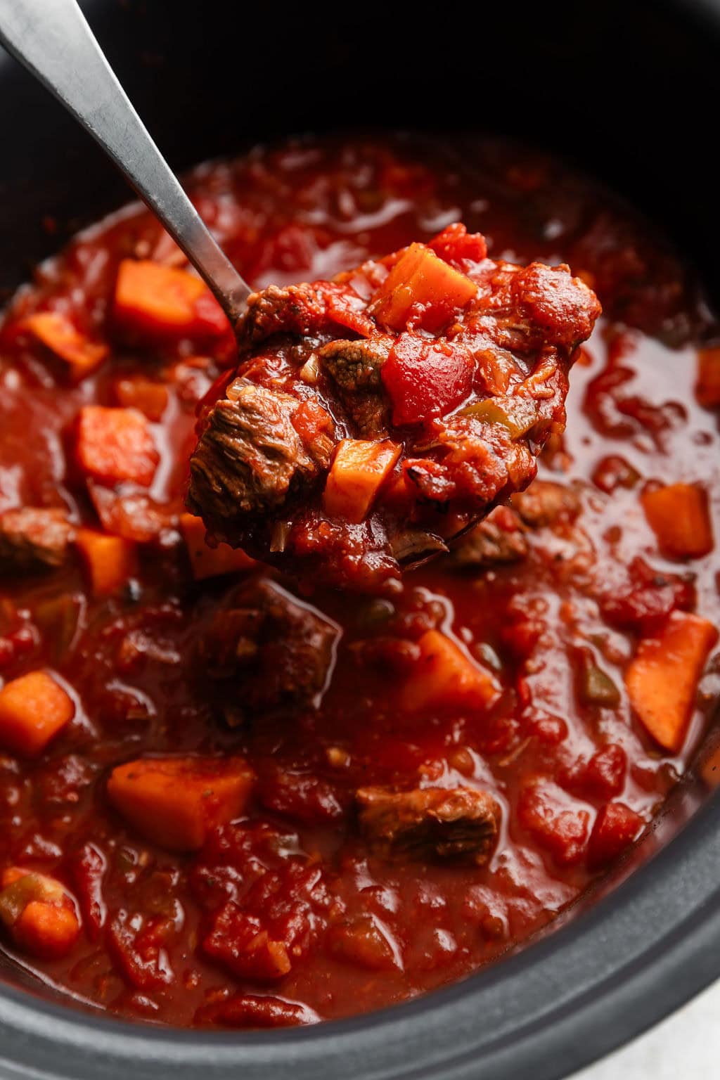 Close up view of a slow cooker filled with Slow Cooker Chuck Roast Chili with Sweet Potatoes being scooped with a spoon.