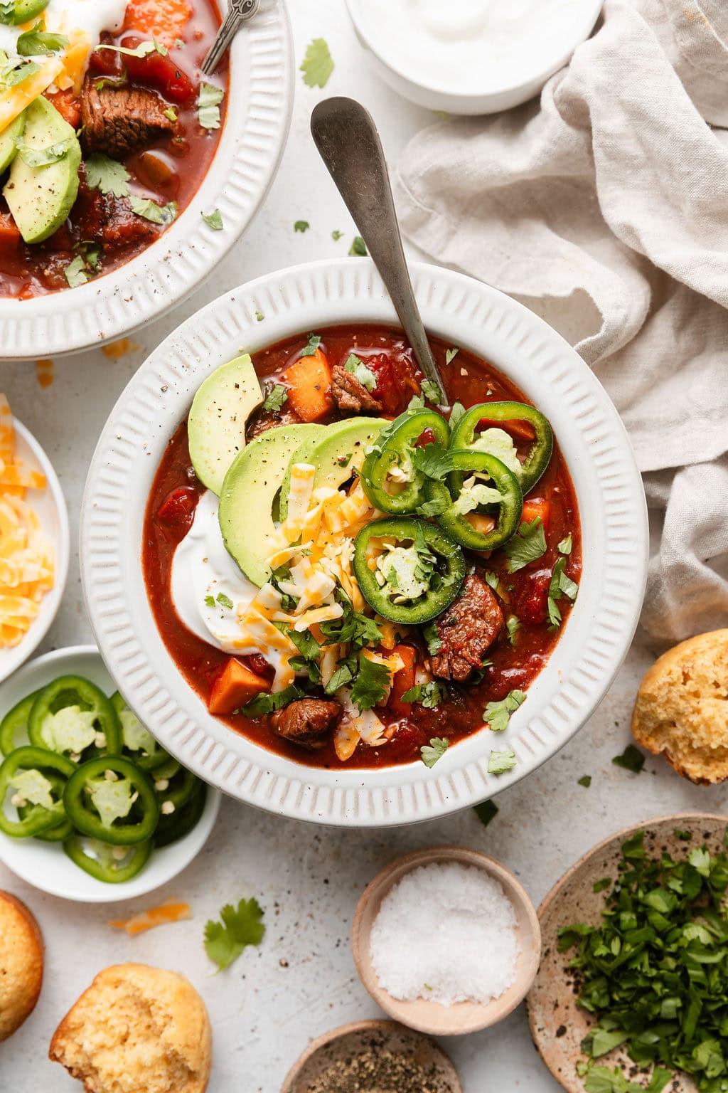 Overhead view of a white bowl of Slow Cooker Chuck Roast Chili with Sweet Potatoes topped with avocado pieces and shredded cheese.