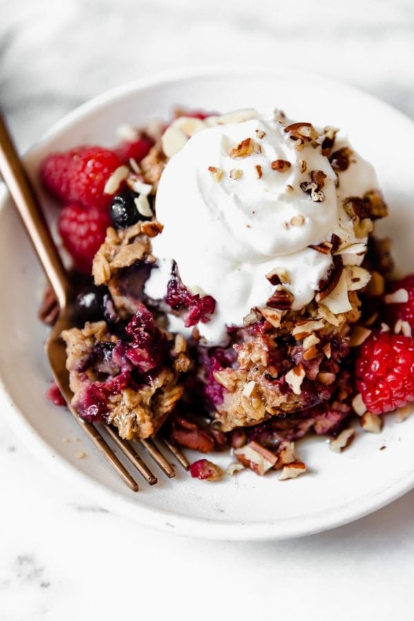 Overhead view of a bowl of mixed berry baked oatmeal topped with whipped cream and pecan pieces. 