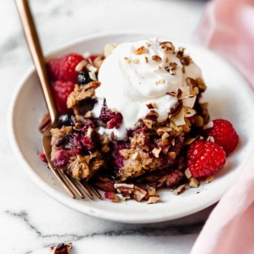 A white plate filled with a piece of Mixed Berry Baked Oatmeal topped with whipped cream