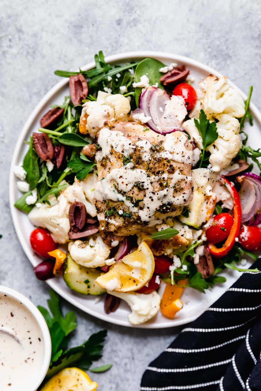 Overhead view white plate filled with serving of Mediterranean chicken served over spinach and roasted vegetables