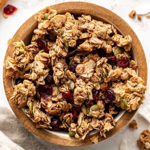 Overhead view of a bowl of homemade granola showing the crunchy texture and pieces of dried fruit throughout the pieces.