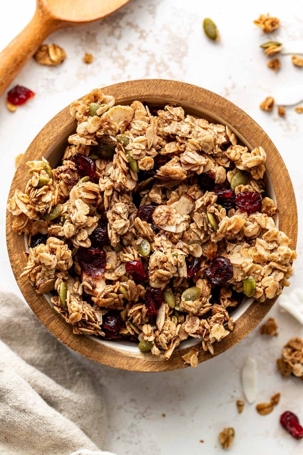 Overhead view of a small wooden bowl filled with Homemade Granola showing the crunchy texture and dried fruit pieces throughout the mixture.