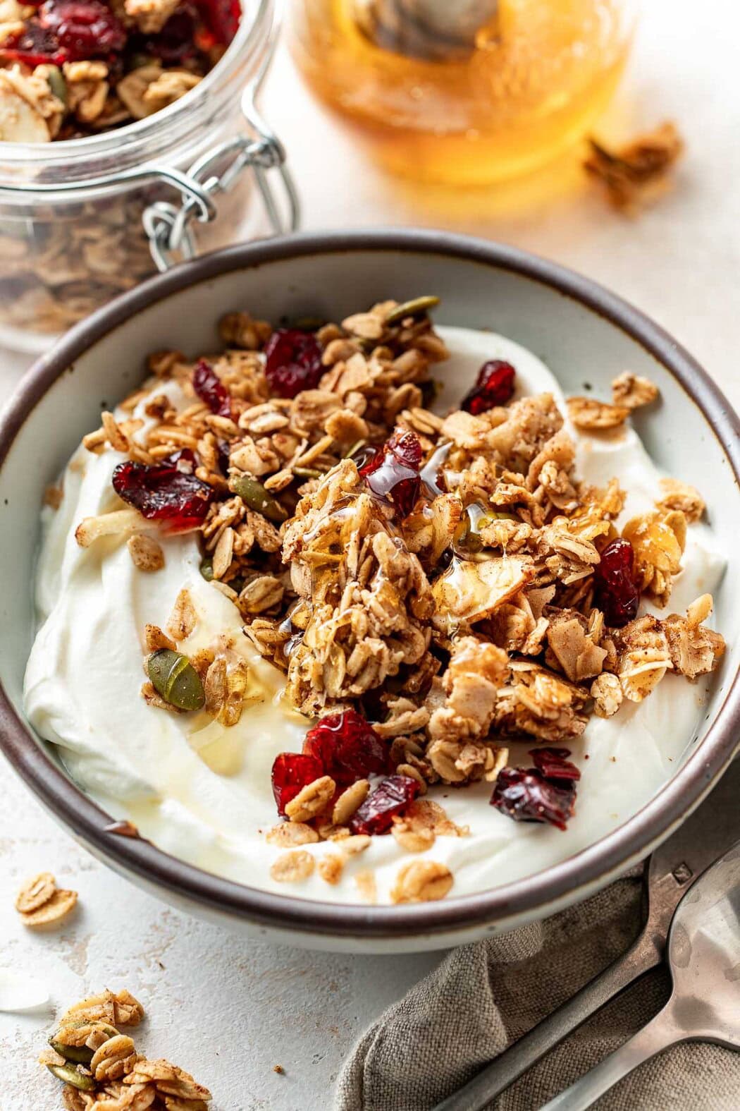 Close up view of a bowl of yogurt topped with Homemade Granola and drizzled with honey on top.