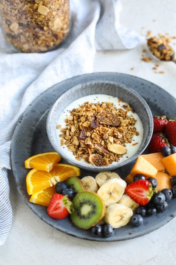 A bowl of Maple Cinnamon Granola on top of yogurt surrounded by fresh fruit