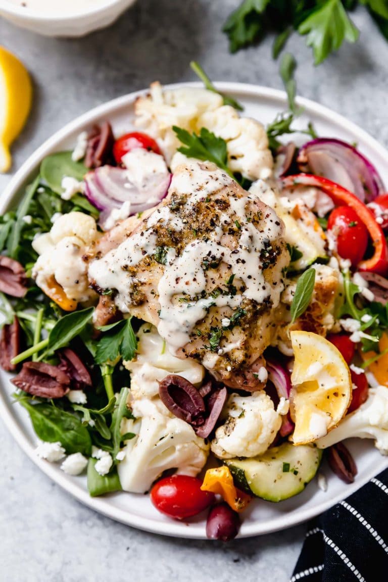 Overhead view of a plate of mediterranean chicken and veggies topped with a lemon-tahini dressing. 