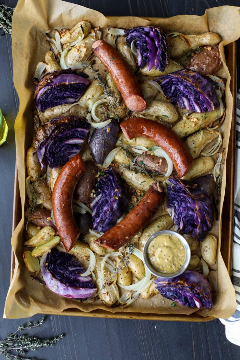 Overhead view of a sheet pan filled with kielbasa, cabbage, and potatoes with a side of whole grain mustard.