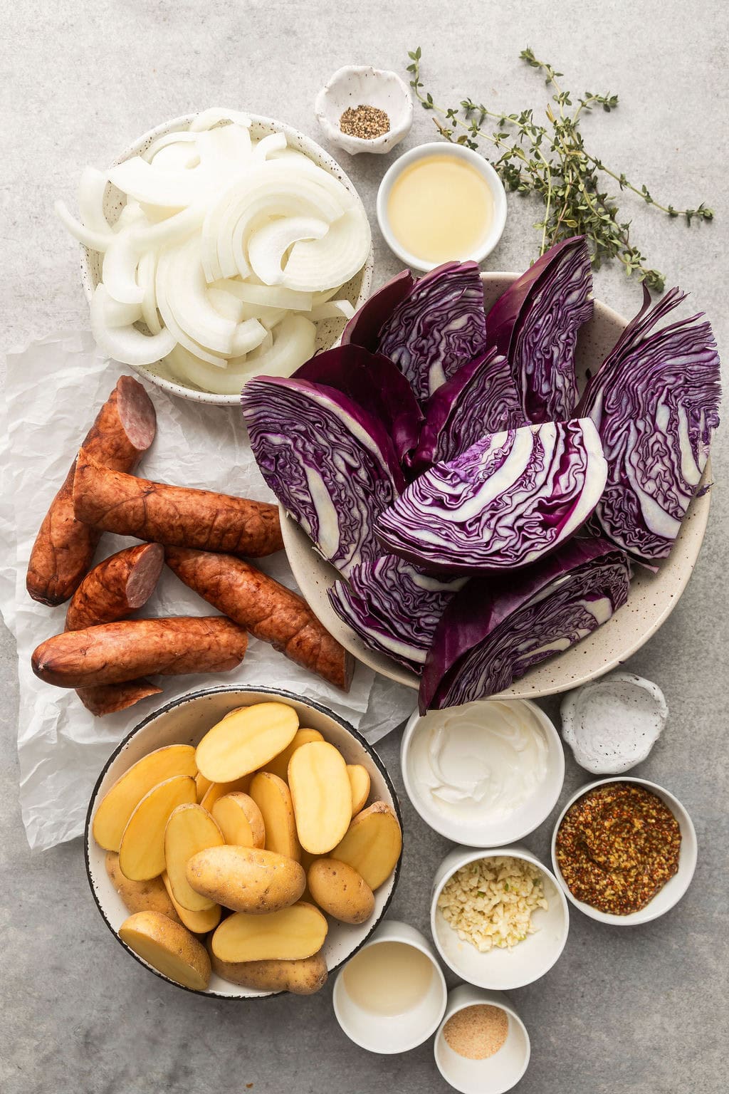 Overhead view of a variety of ingredients for Sheet Pan Kielbasa and Potatoes in different sized bowls.