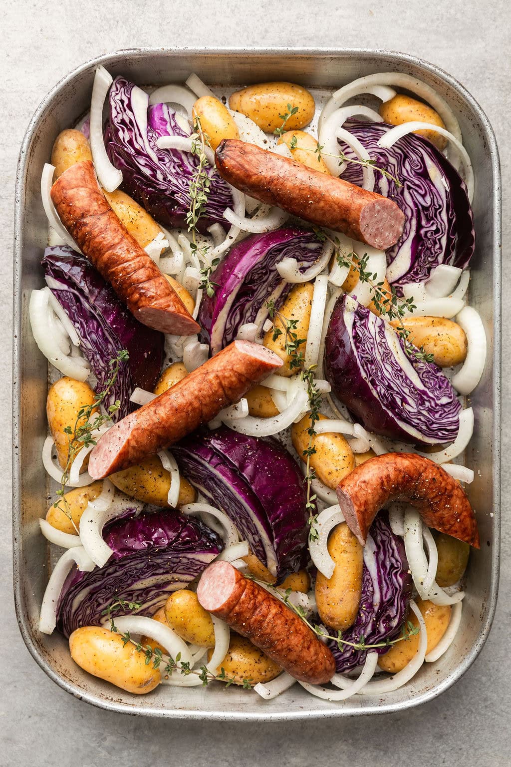 Overhead view of a Sheet Pan filled with Kielbasa and Potatoes topped with fresh herbs and black pepper.
